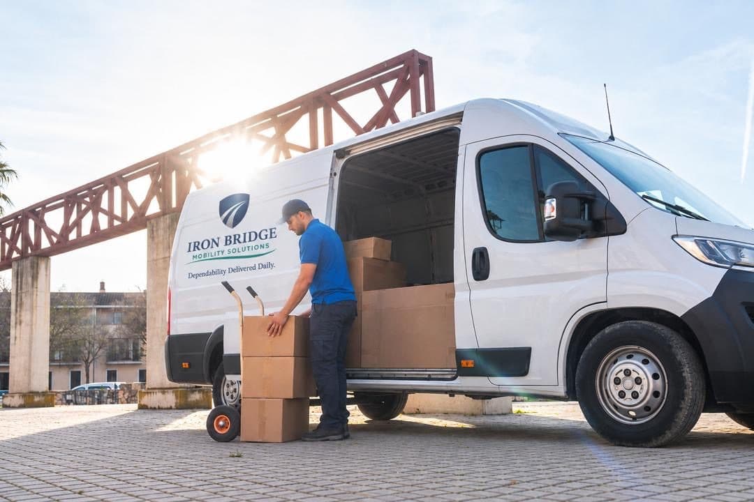 Iron Bridge driver unloading boxes from a branded cargo van onto a hand truck